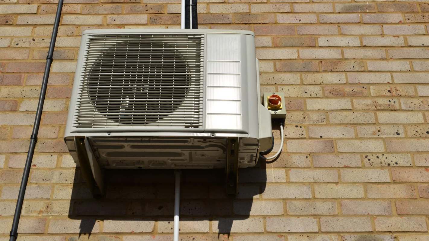 An air conditioning unit mounted on a brick wall with electrical connections.