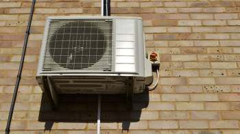 An air conditioning unit mounted on a brick wall with electrical connections.
