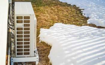 An air conditioning unit is positioned next to a patch of snow and brown grass.