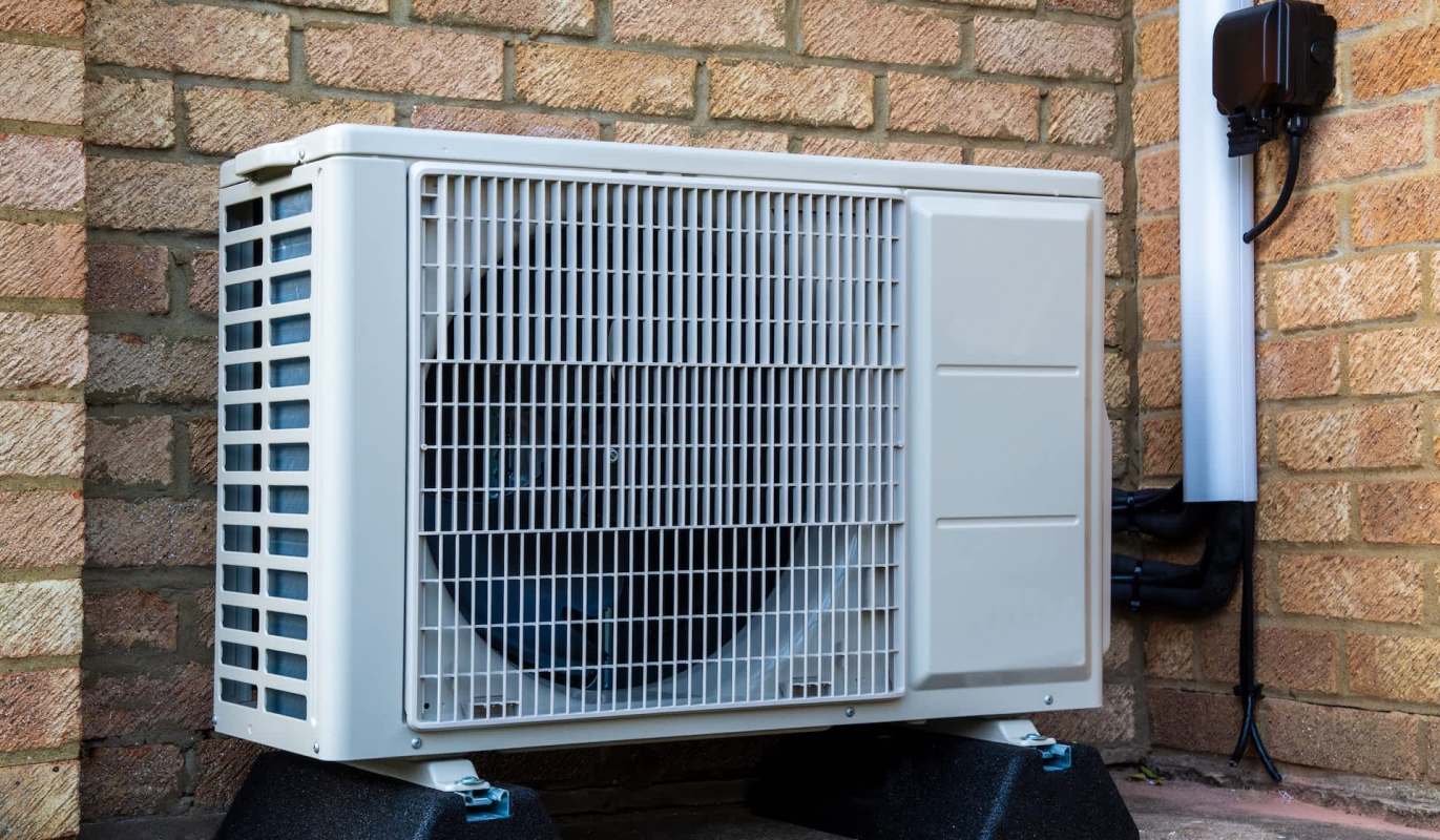 An outdoor air conditioning unit mounted against a brick wall.