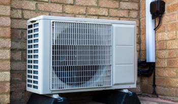 An outdoor air conditioning unit mounted against a brick wall.