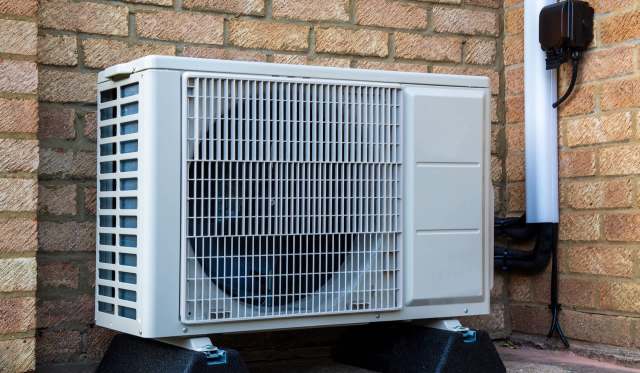 An outdoor air conditioning unit mounted against a brick wall.