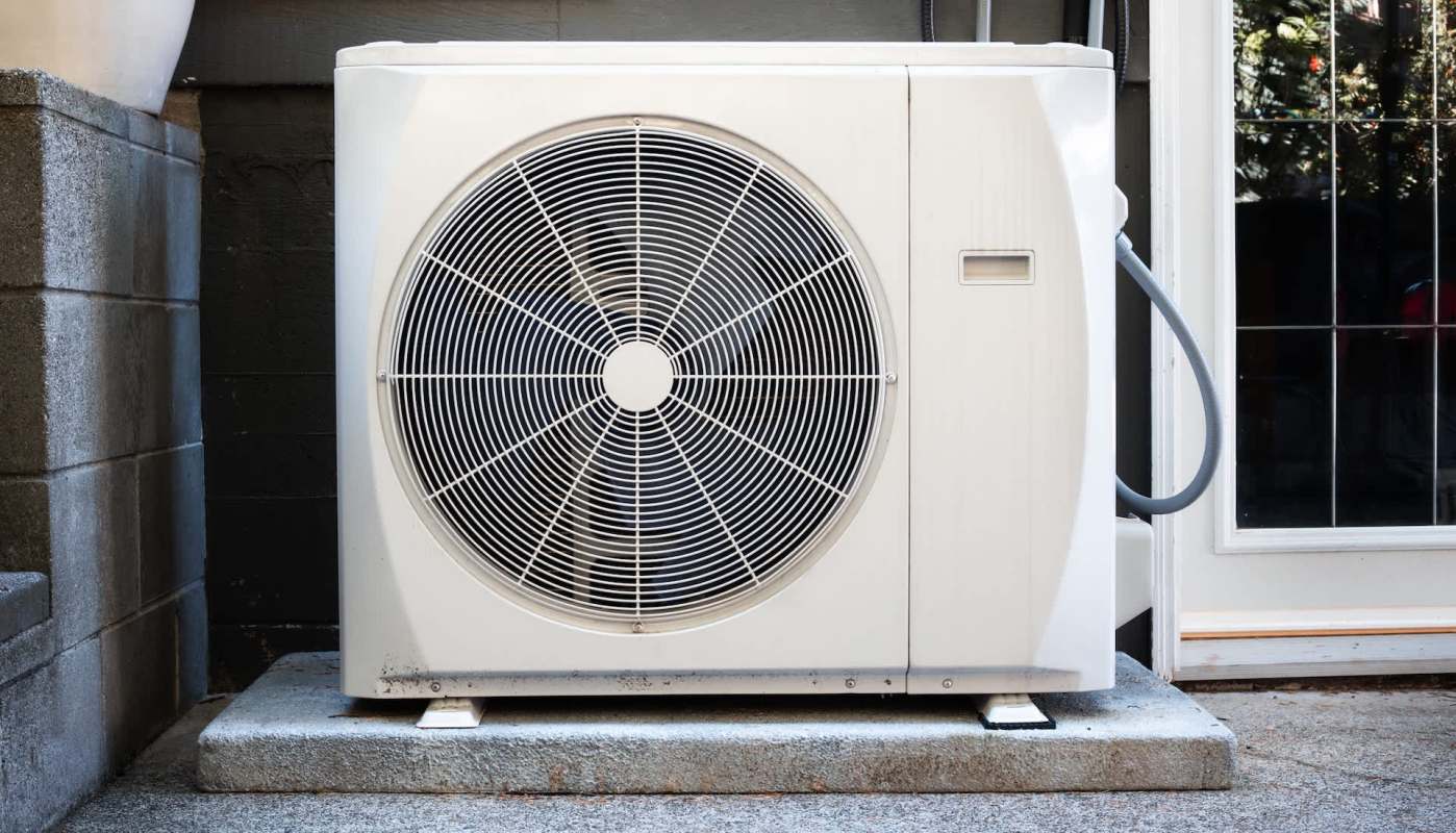 An outdoor air conditioning unit placed on a concrete slab next to a building.