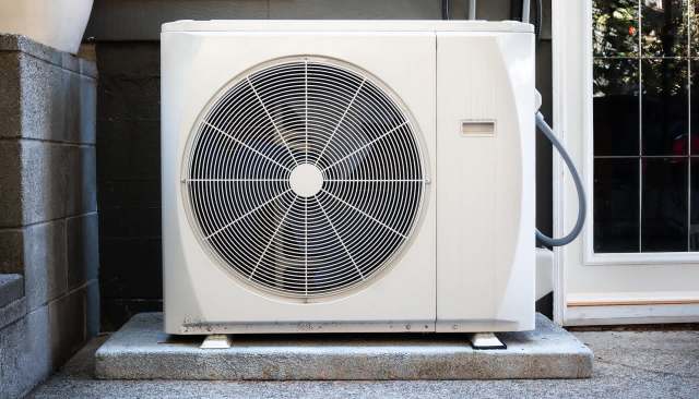 An outdoor air conditioning unit placed on a concrete slab next to a building.