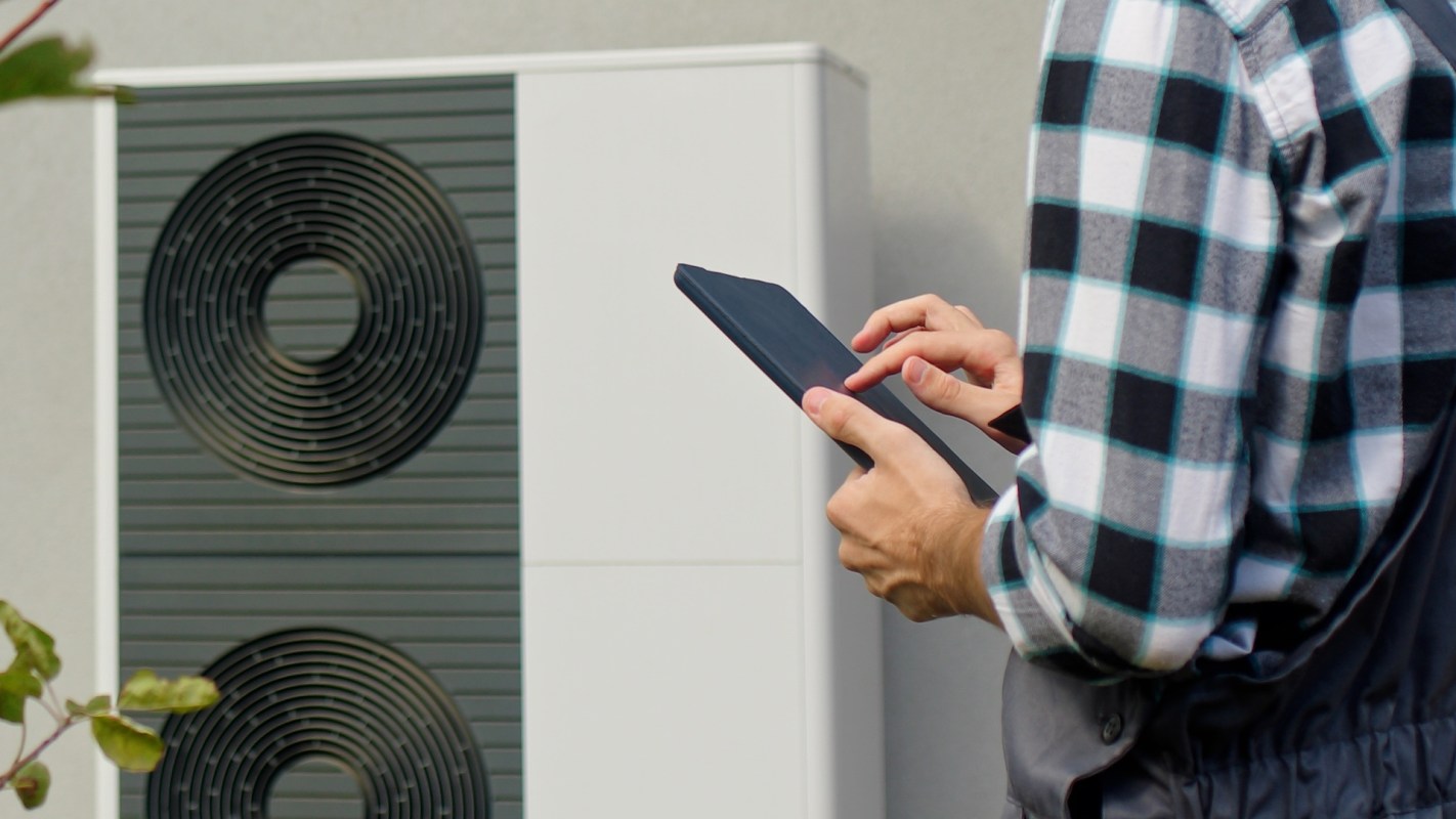 A person using a tablet next to a wall-mounted air conditioning unit.