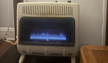 A gas heater with a blue flame, enclosed in a metal grid, situated near a wooden table.