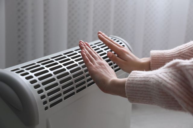 A woman heating her hands on an electric heater.