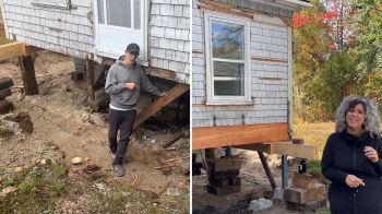 Two people stand near a house elevated on support beams with exposed foundation work.