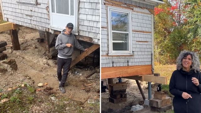 Two people stand near a house elevated on support beams with exposed foundation work.
