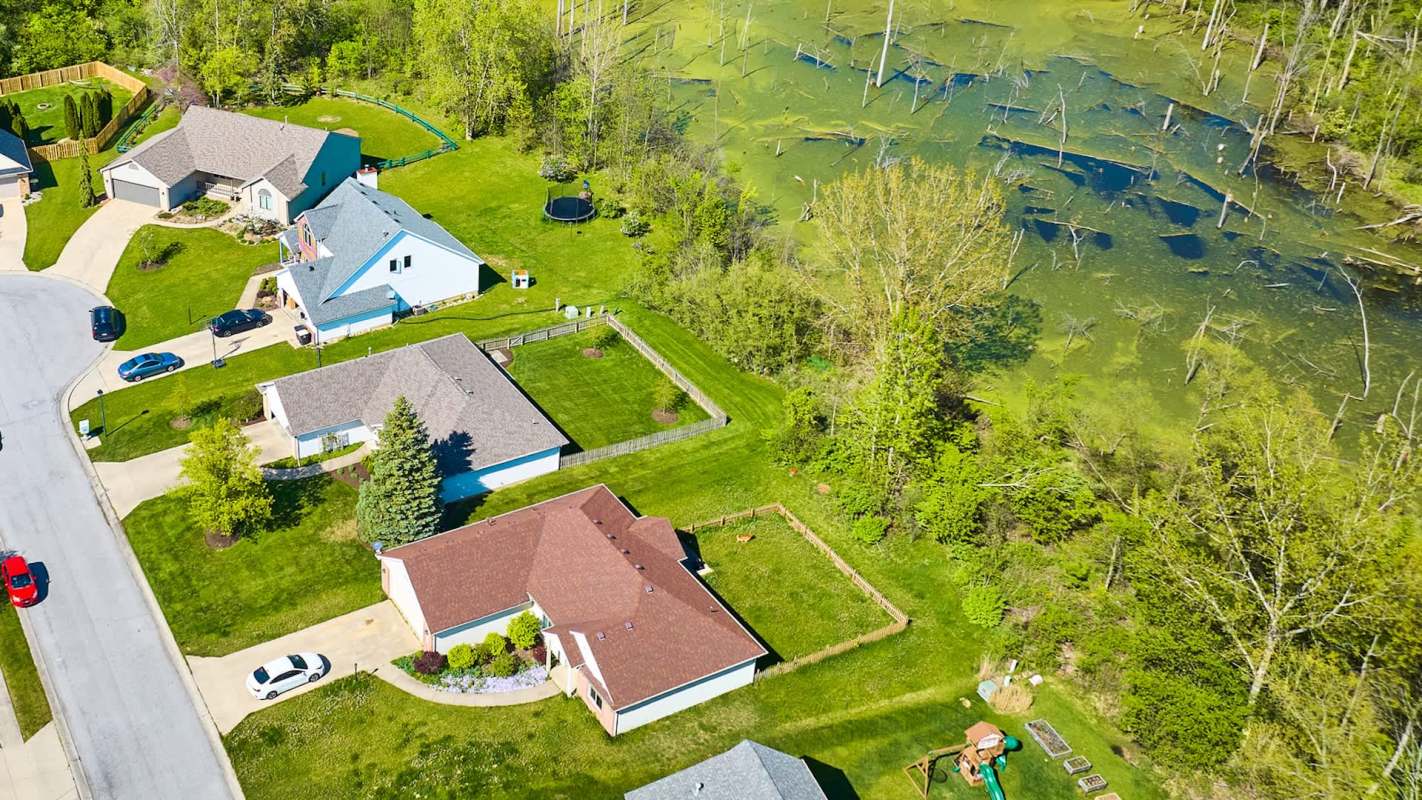 Aerial view of residential houses, yards, and a swamp with trees in a suburban area.