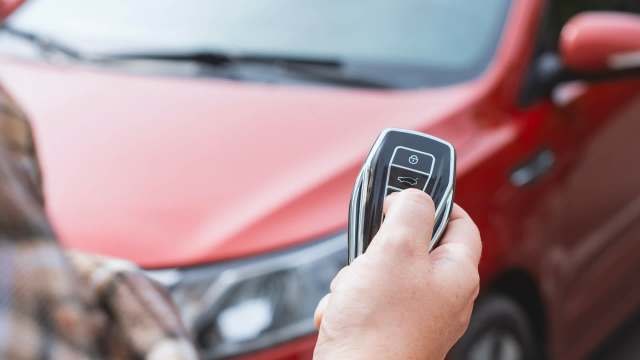 A person holds a car key fob near a red vehicle.