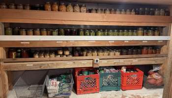 A wooden shelf filled with various jars of canned goods and crates of food items.