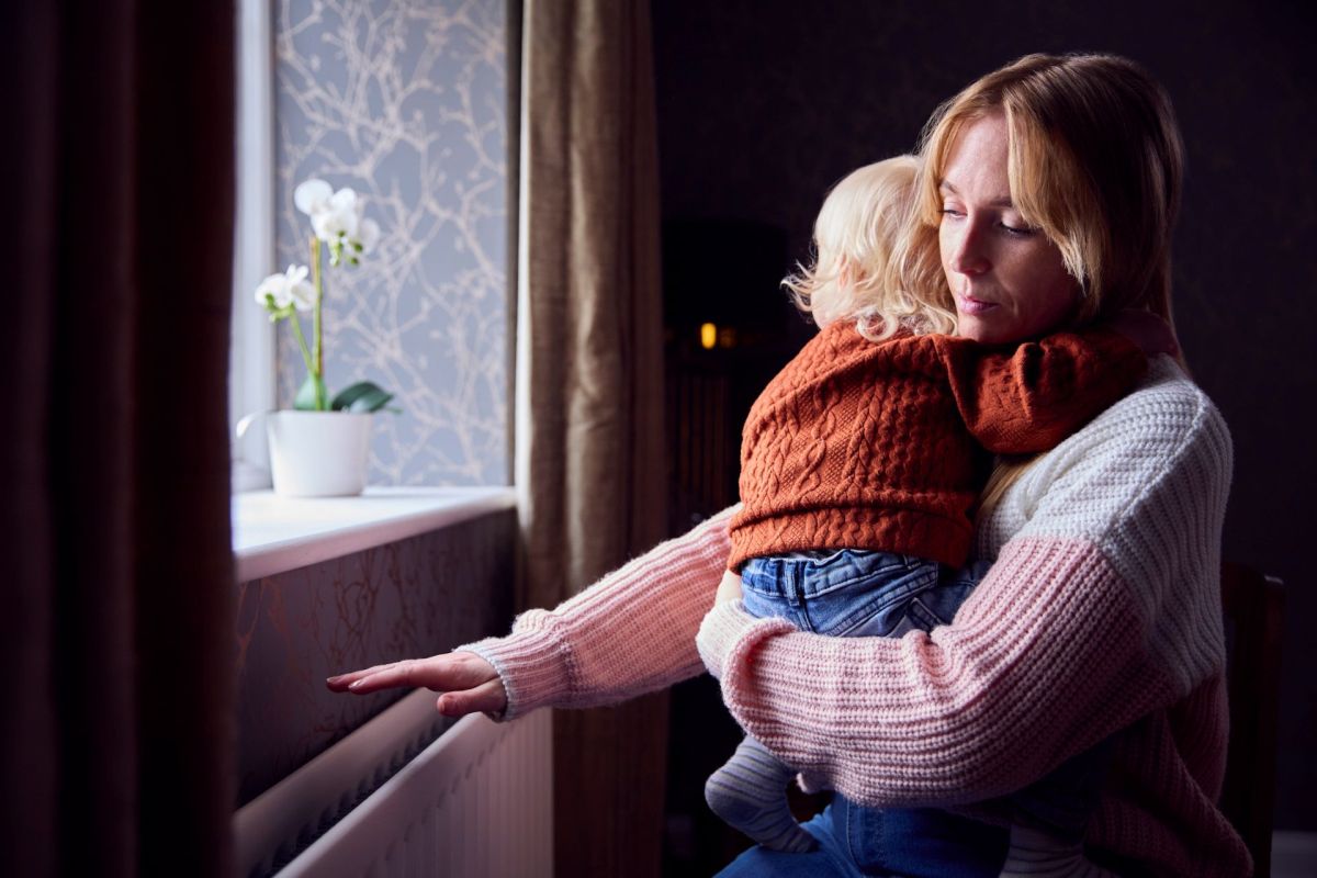 A woman holding a child while putting her hand over a radiator.