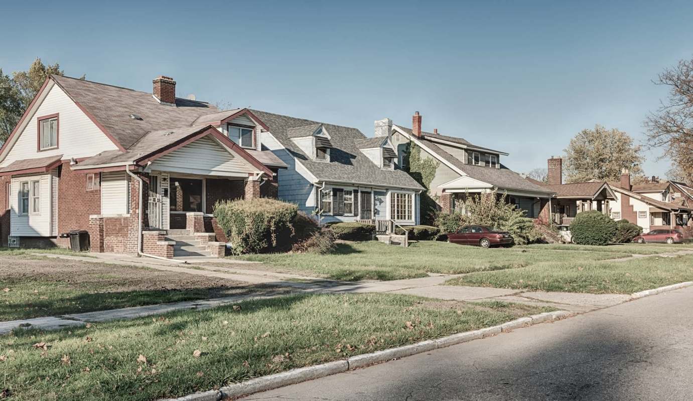 A row of residential houses along a quiet street with grassy lawns.