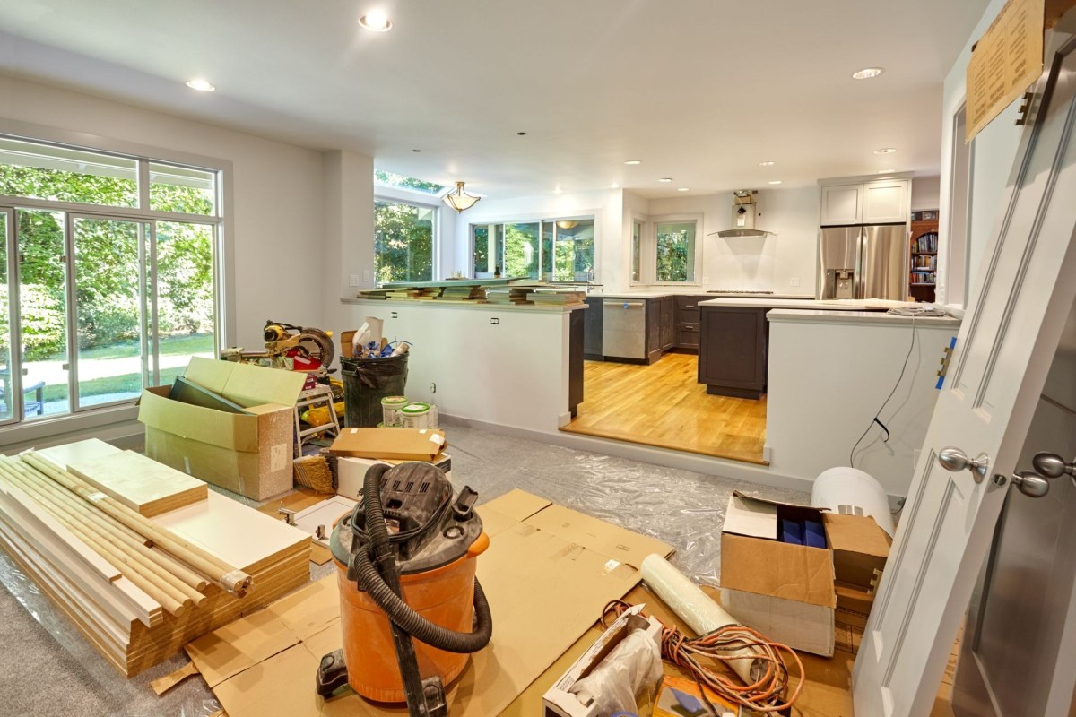 A room under renovation with construction materials, tools, and an unfinished kitchen area.
