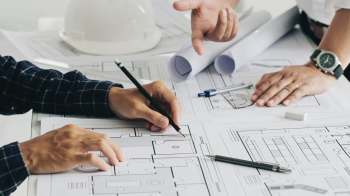 Two people discussing building plans on a table covered with architectural drawings and a hard hat.