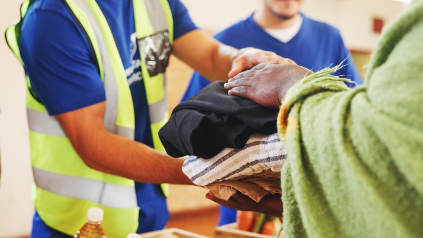 A person hands a stack of clothes to another person during a charitable event.