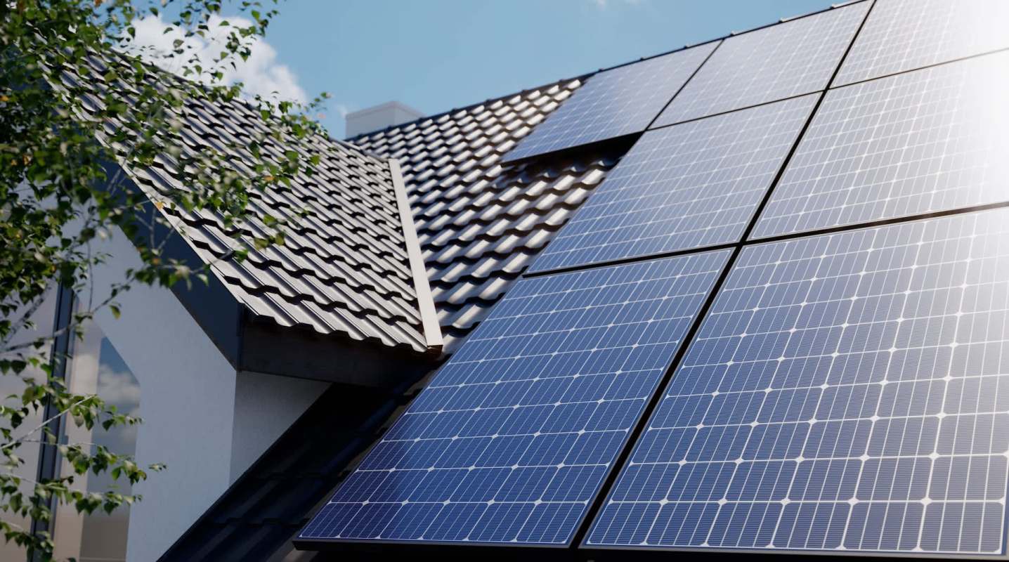 Solar panels installed on a tiled roof with greenery nearby.