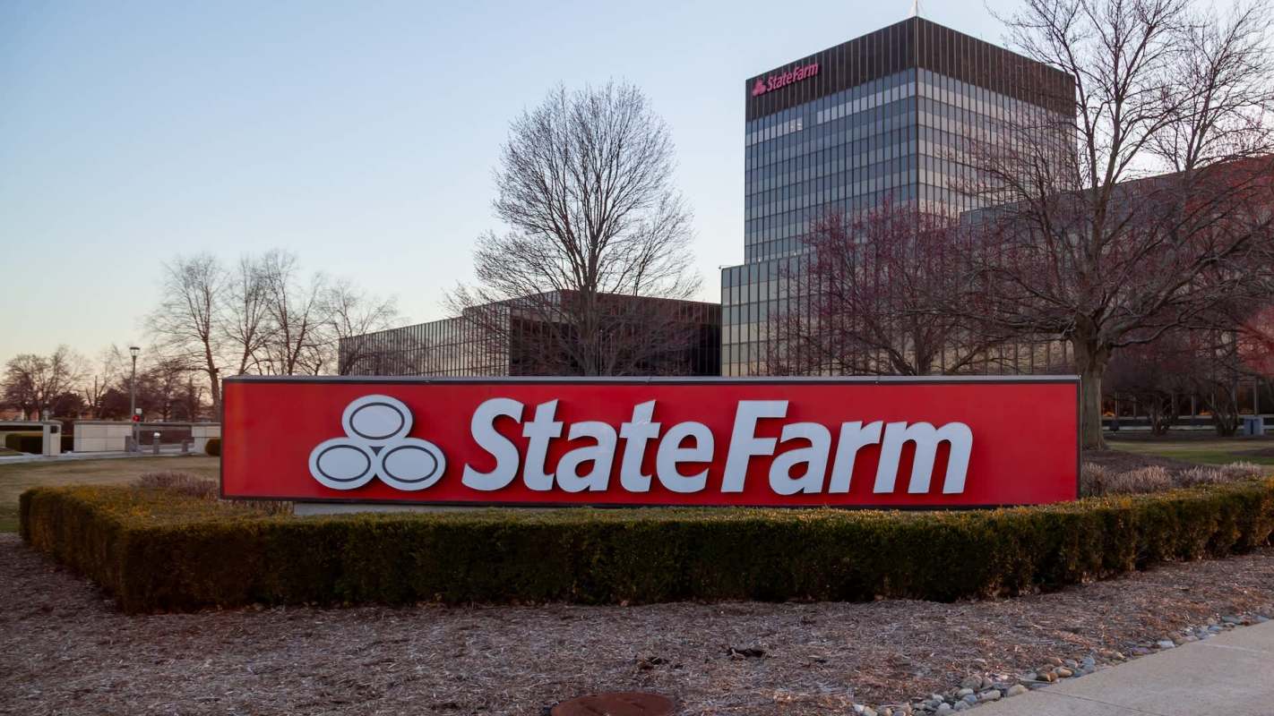 A State Farm sign in front of a corporate building with trees and landscaped shrubs.