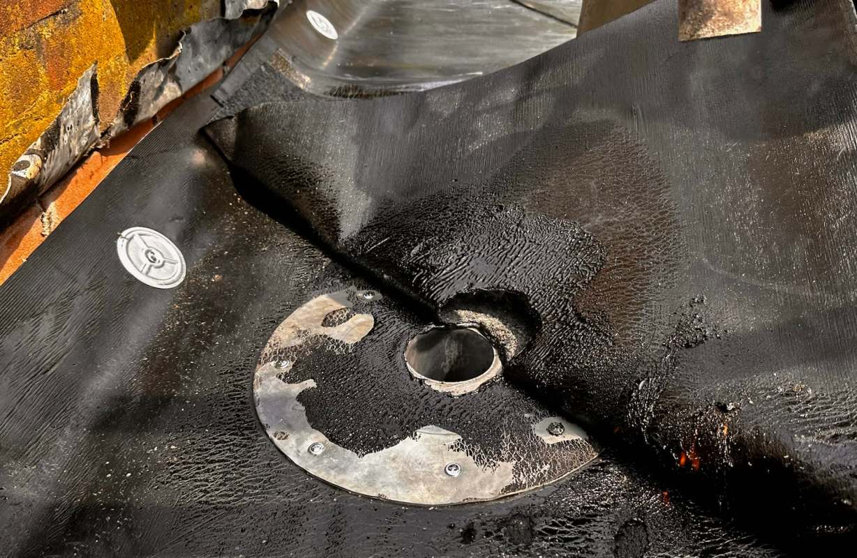 A textured roof with a circular metal fixture and a hole, partially covered by a black material.