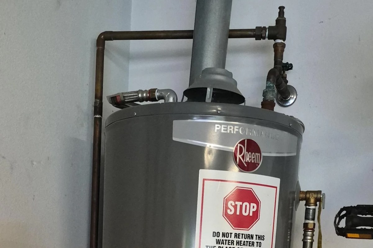 A water heater with pipes and a warning sign attached to it.