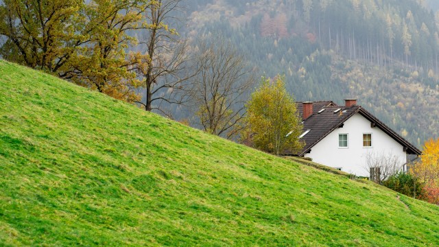 A house on a hillside surrounded by trees and mountains.