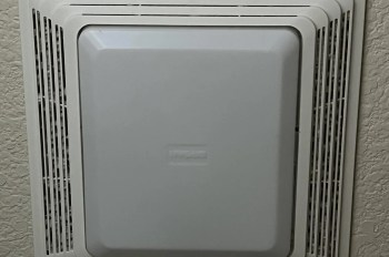 A white wall-mounted ceiling bathroom fan with a rectangular cover and ventilation grilles.