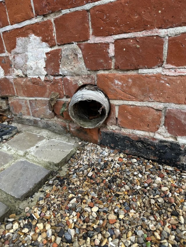 A dryer vent sticking out of a brick wall. 