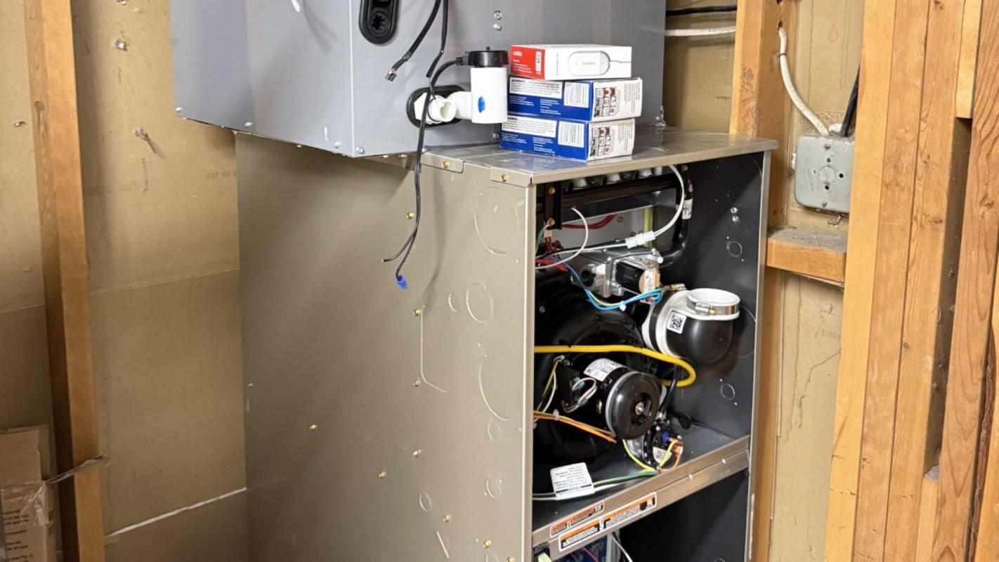 A furnace and air conditioning unit in a utility room with visible wiring and plumbing components.