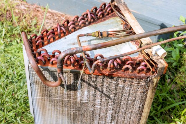 An old, rusted condenser coil with copper tubes surrounded by grass.