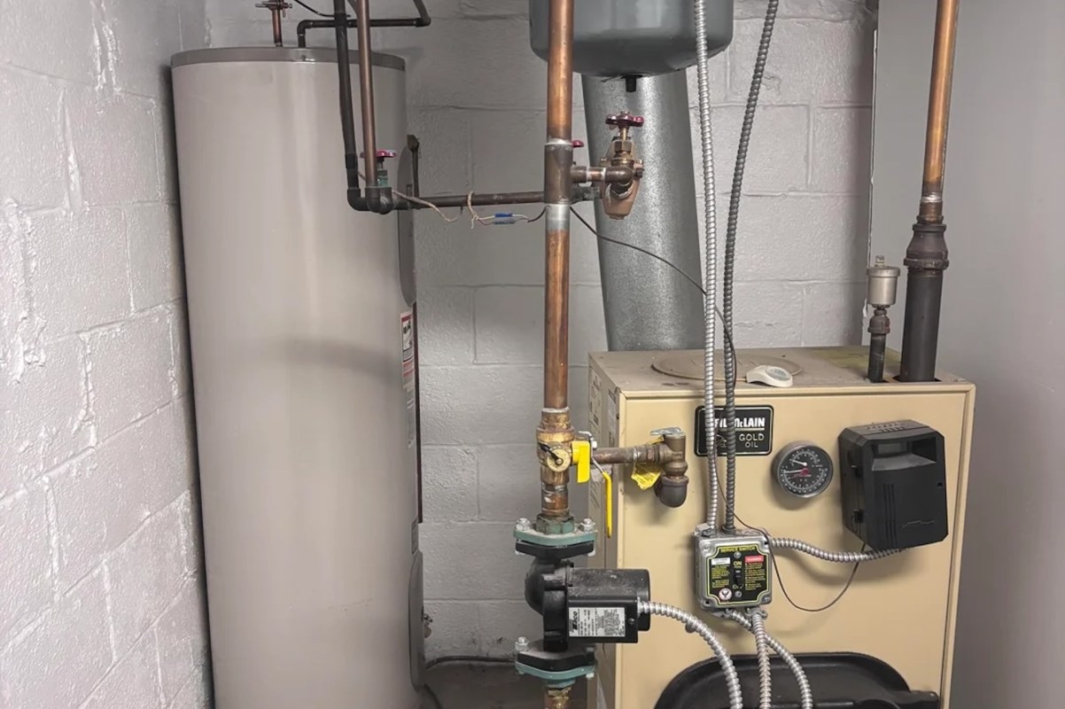 A water heater and oil furnace with pipes and valves in a utility room.
