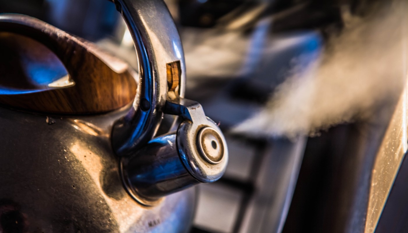 A kettle with steam rising from its spout on a kitchen stovetop.
