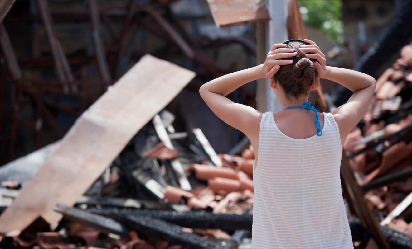 A person stands among rubble and debris from a burned structure.