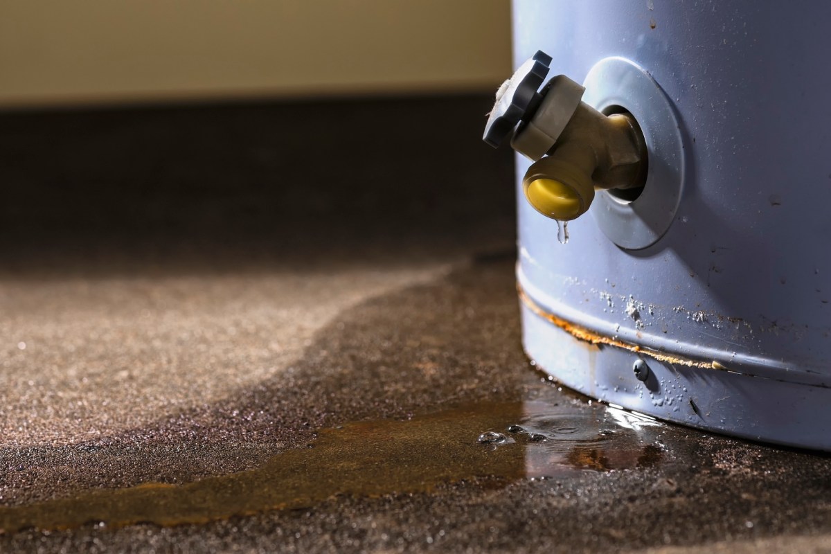A leaking water valve attached to a blue tank with a puddle forming on the ground.