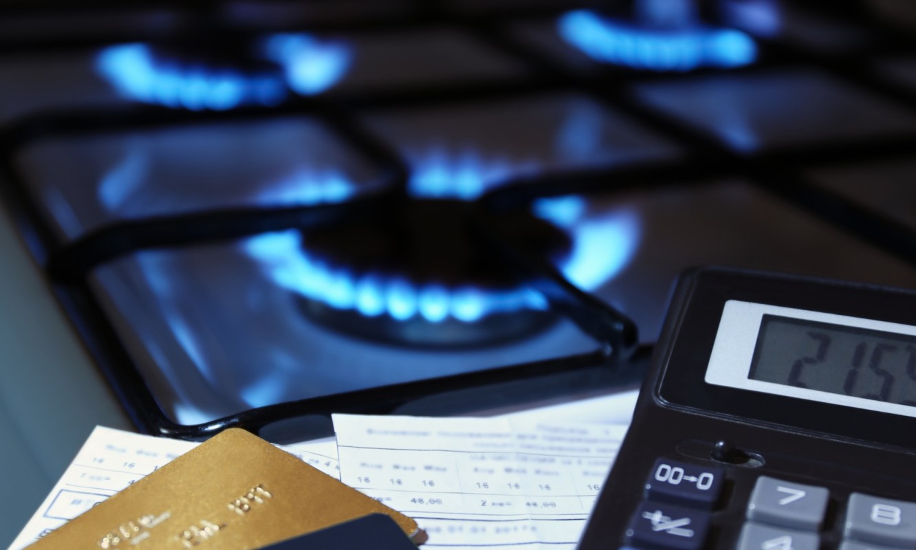 Gas stove burners with blue flames, a calculator, and utility bills on a countertop.