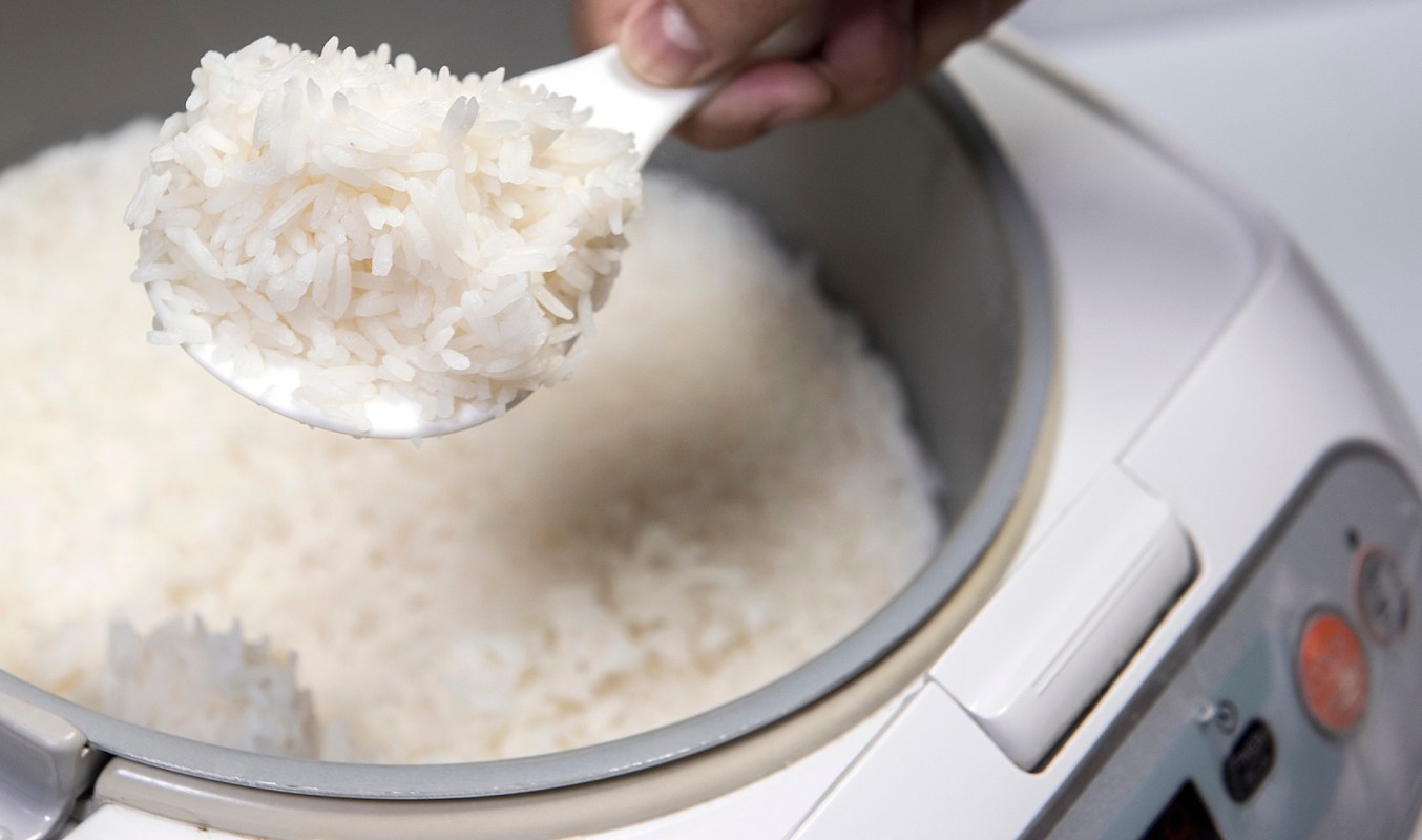 A spoonful of cooked rice is being lifted from a rice cooker.