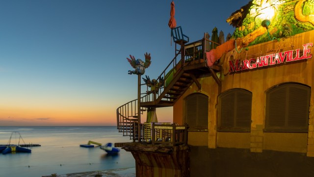 A colorful Margaritaville restaurant building with a staircase and water activities in the ocean at sunset.