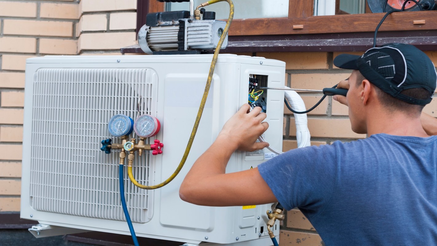 A person repairs an air conditioning unit mounted on a wall.