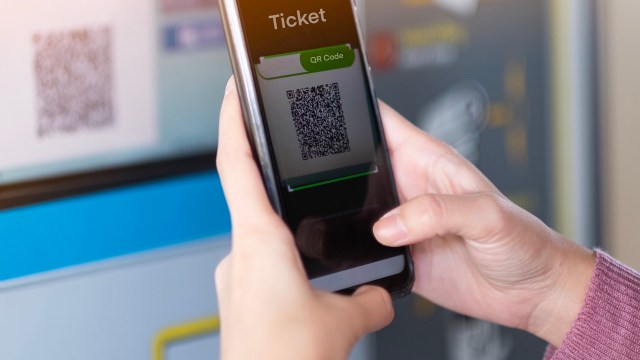 A person scans a QR code on a smartphone in front of a ticket machine.