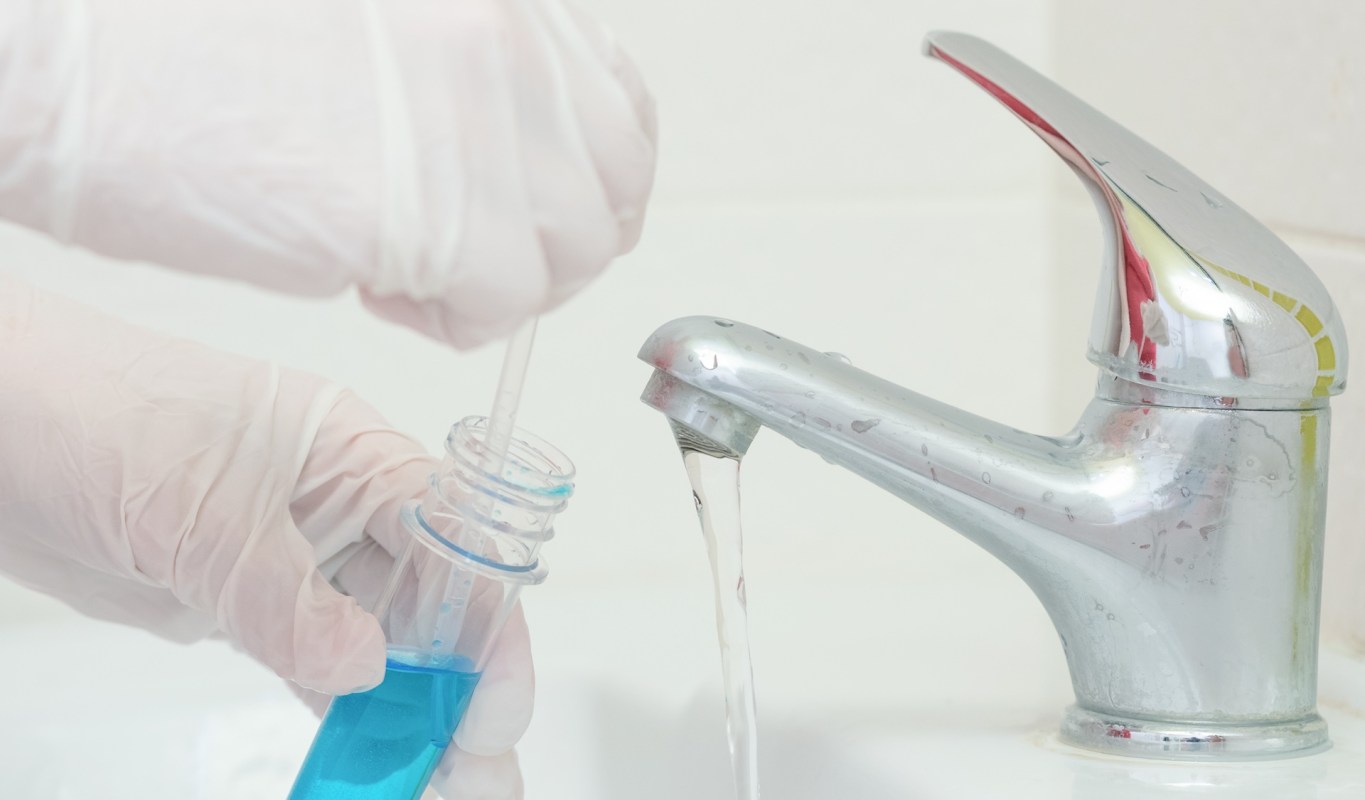 Gloved hands collecting a tap water sample.