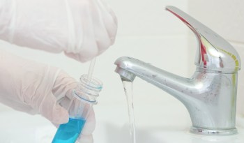 Gloved hands collecting a tap water sample.