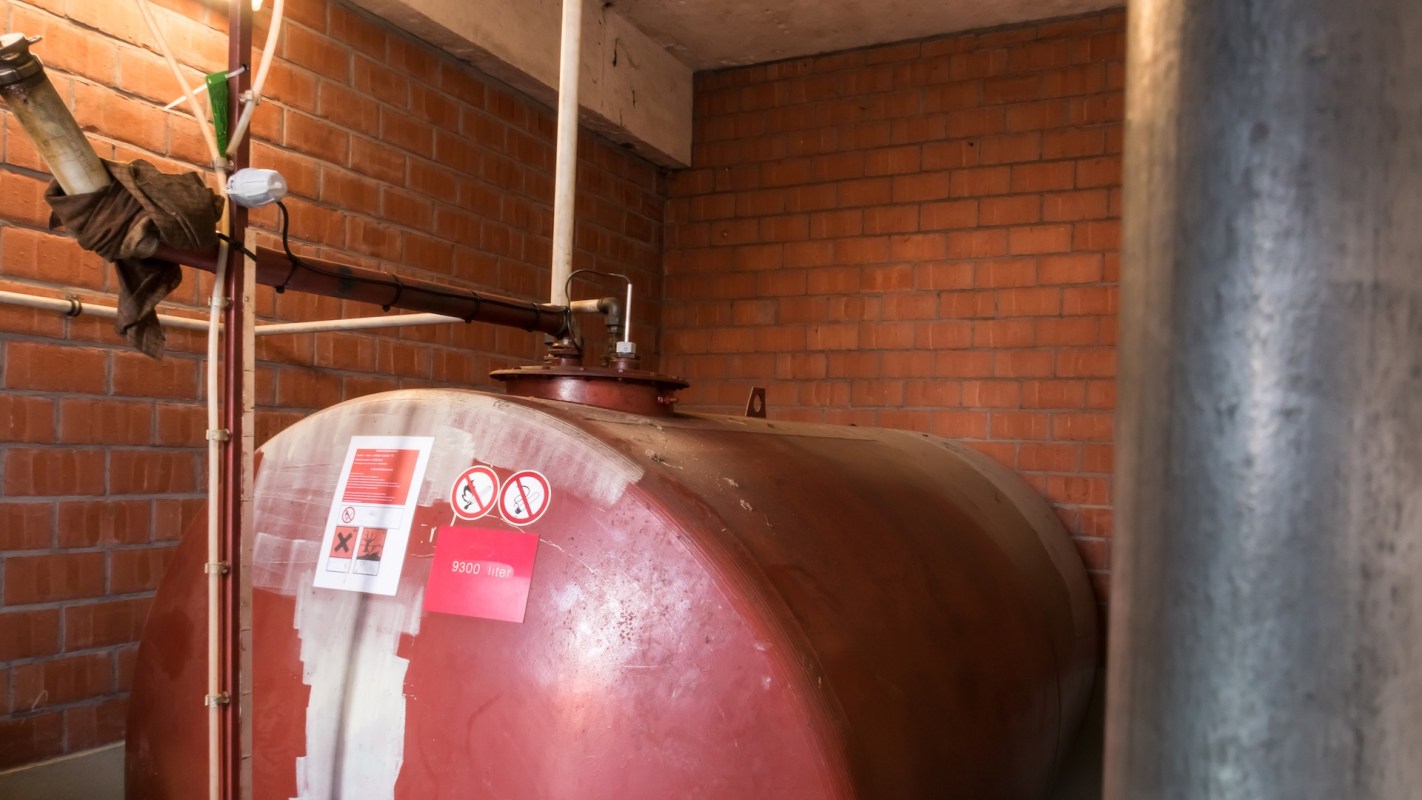 A large red industrial oil storage tank with warning labels in a brick-walled room.
