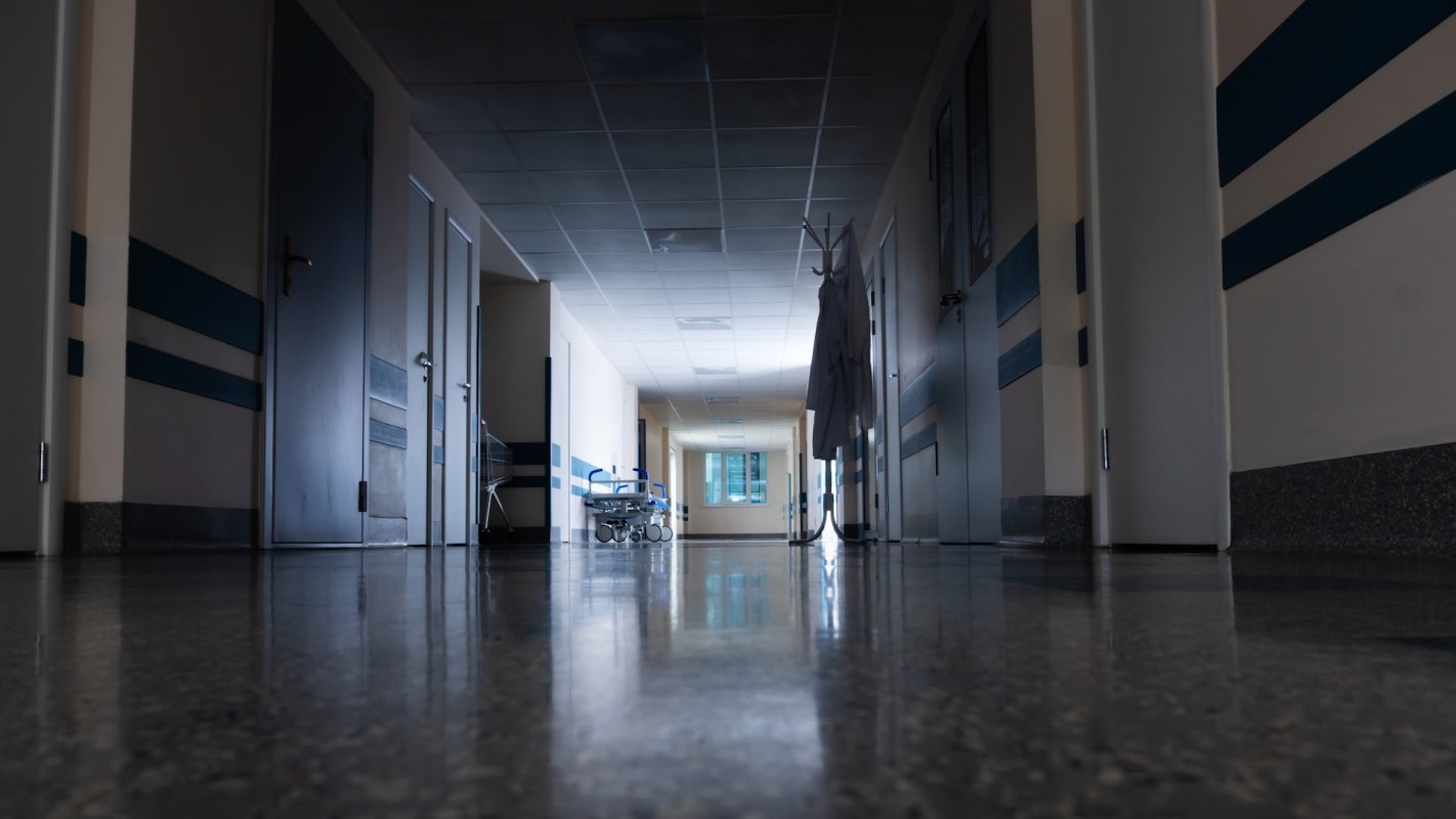 A dark hospital corridor with several doors and a cart in the distance.