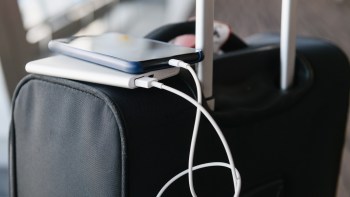 A smartphone and a portable charger are resting on top of a suitcase, connected by a charging cable.