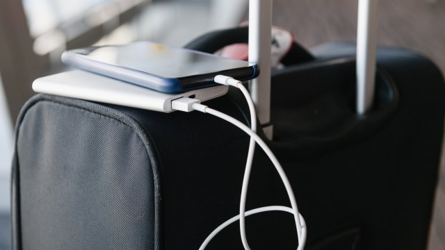 A smartphone and a portable charger are resting on top of a suitcase, connected by a charging cable.