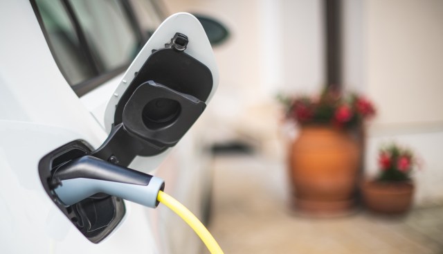 An electric vehicle charging with a yellow cable connected at a charging port at a home.