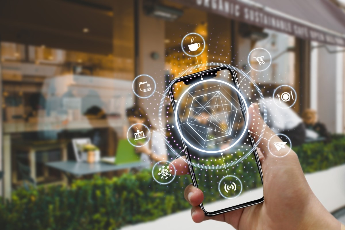 A hand holding a smartphone displays digital icons related to food and services outside a café.