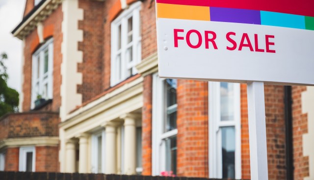 A "For Sale" sign in front of a brick building with large windows.