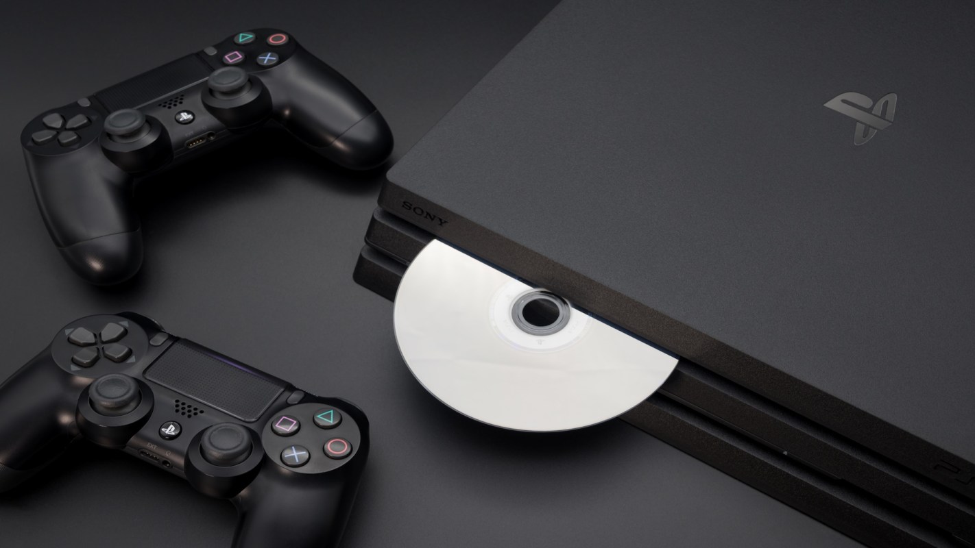 A PlayStation console with a disc inserted and two black controllers beside it.