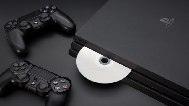 A PlayStation console with a disc inserted and two black controllers beside it.